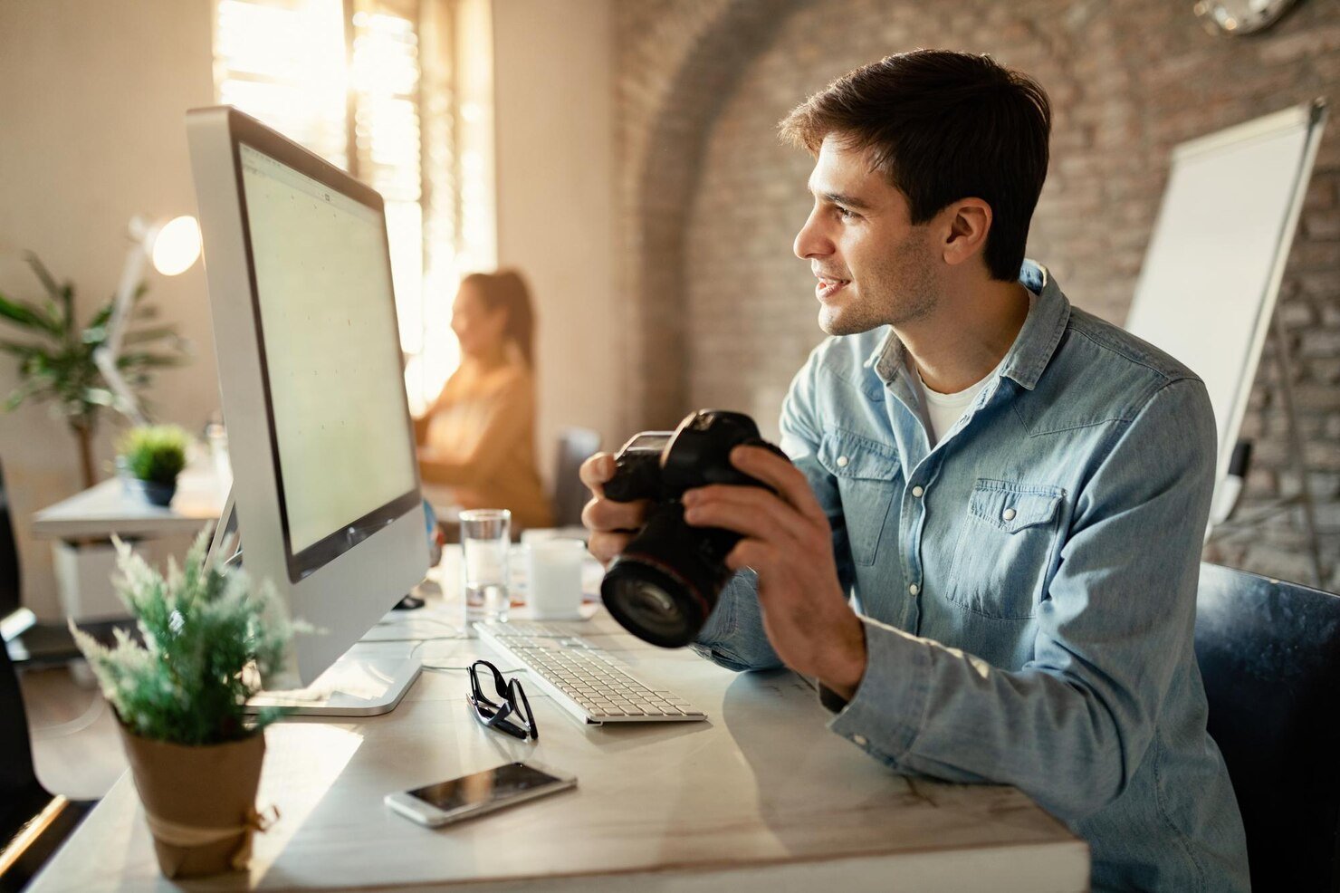 smiling-design-professional-with-photo-camera-working-desktop-pc-studio_637285-2778